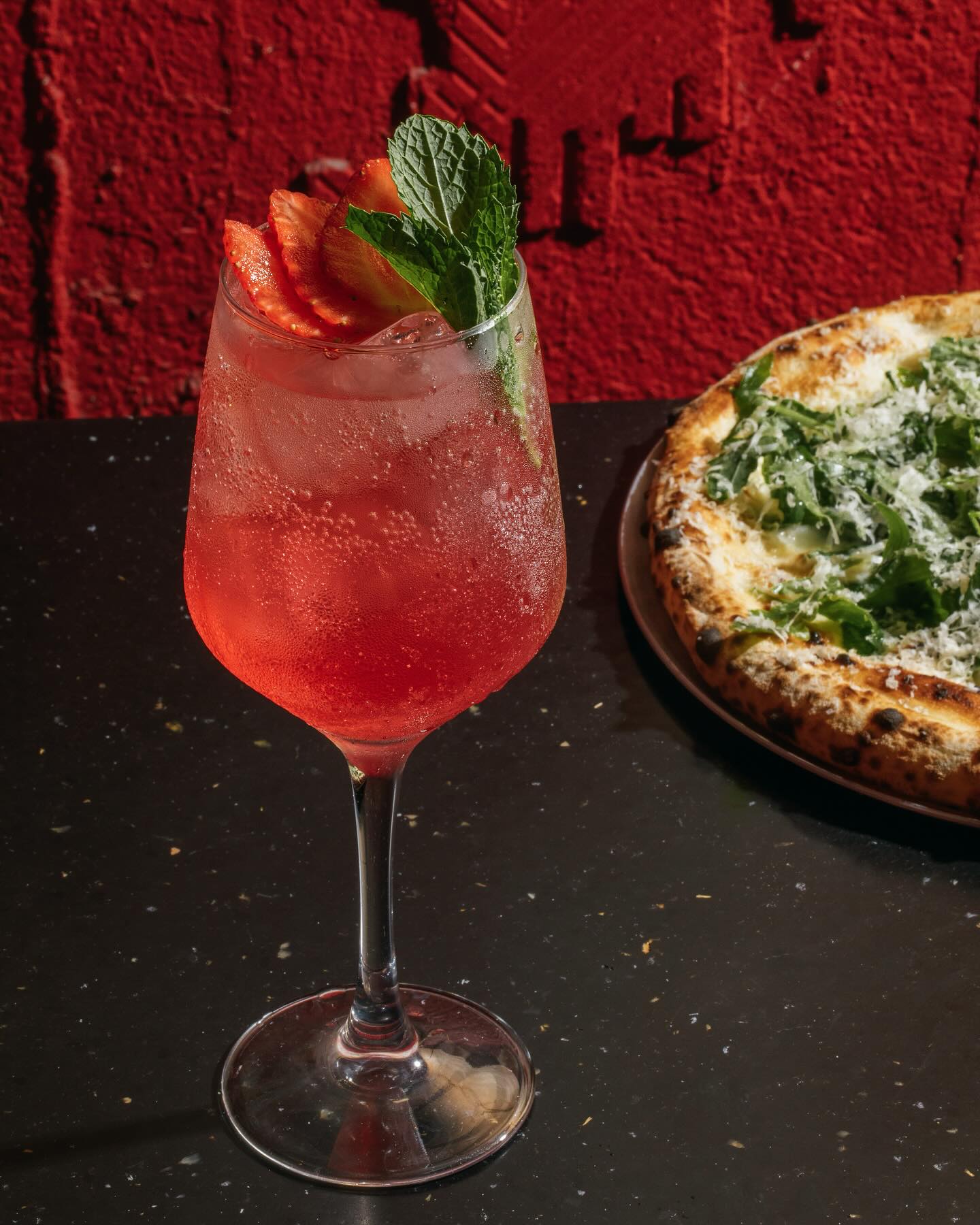 Spritz and pizza against a red wall